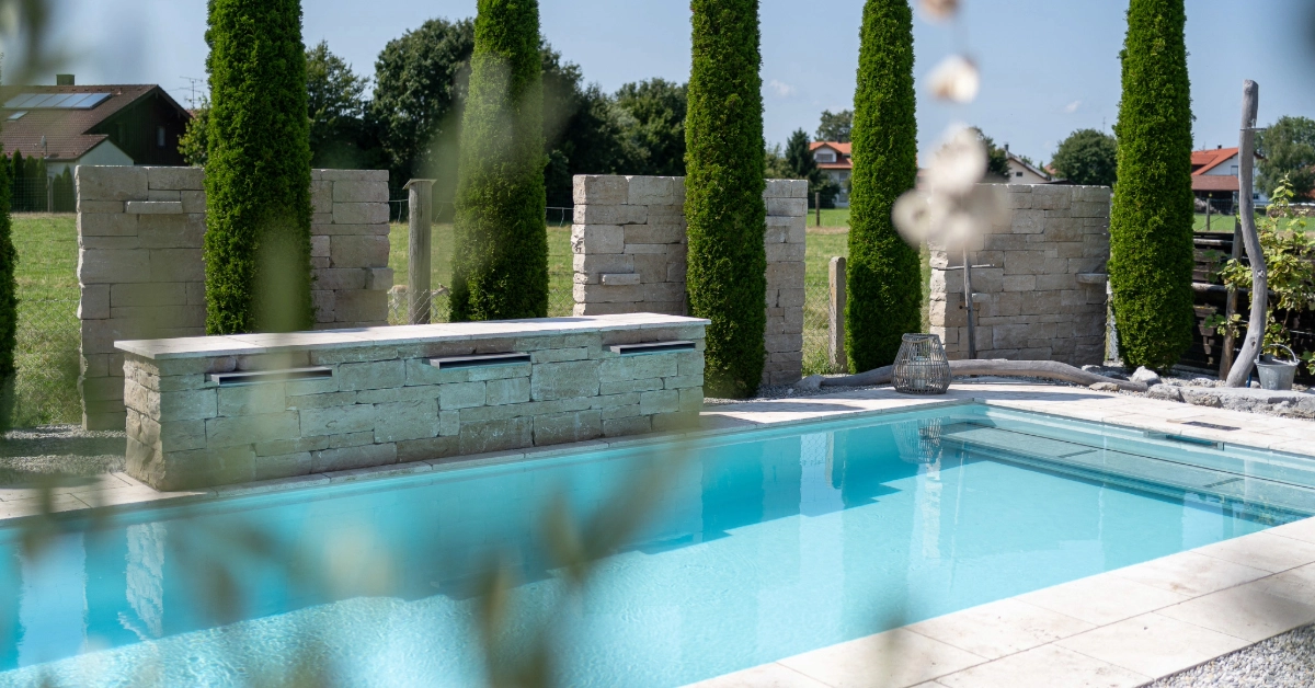 Poolanlage mediterran mit türkiser Wasserfarbe und Naturstein Poolumrandung und Wasserfälle inklusive Sichtschutzmauern